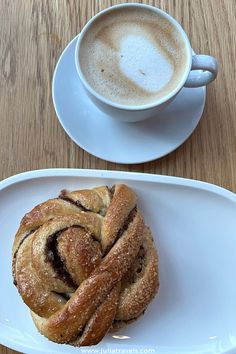 a pastry on a plate next to a cup of cappuccino and saucer