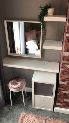 a small white desk with a mirror and stool in front of the window, next to a brick wall