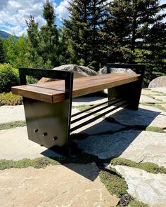 a wooden bench sitting on top of a stone floor next to some trees and rocks