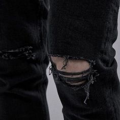 a person wearing black ripped jeans with holes on their legs and one leg in the air