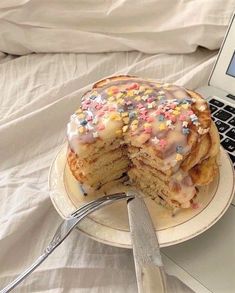 a laptop computer sitting on top of a bed next to a stack of pancakes covered in sprinkles