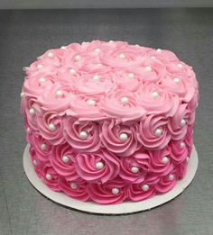 a cake with pink frosting and white pearls on the top is sitting on a plate