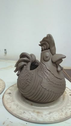 a clay sculpture of a rooster on top of a white table with two other items in the background