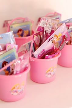 pink plastic buckets filled with princess items on top of a white countertop next to each other