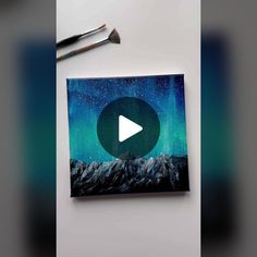 an image of a painting with a video playing button in the center and two paintbrushes next to it