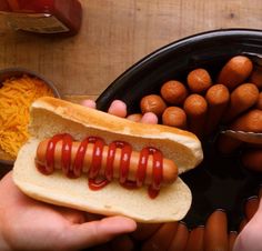 a person holding a hot dog with ketchup and mustard on it next to some buns