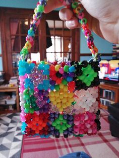 a person holding up a bag made out of plastic beads and other colorful items on a table