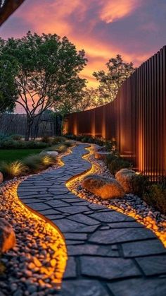 a stone path leading to a fence with trees and bushes in the background at sunset