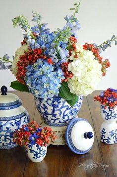 a blue and white vase filled with flowers on top of a wooden table next to two jars