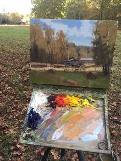 an easel with some paint on it sitting in the grass near a field and trees