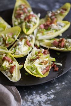 some lettuce cups with bacon and cheese on them sitting on a black plate