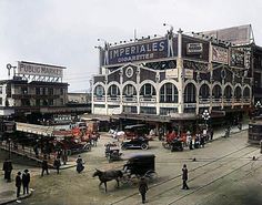 an old photo of people and cars in front of a large building with several stories