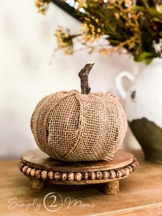 a burlap pumpkin sitting on top of a wooden stand next to a vase with flowers in it