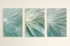 three green and white paintings hanging on a wall in a living room or dining room