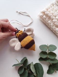 a hand holding a crocheted bee ornament next to some green leaves