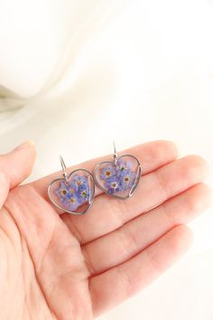 a pair of heart shaped earrings with purple flowers on the front and back of them