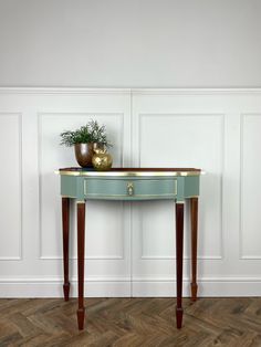 a table with a vase on top of it in front of a white wall and wooden floor