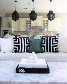 a white couch with black and white pillows on it in a living room next to a kitchen