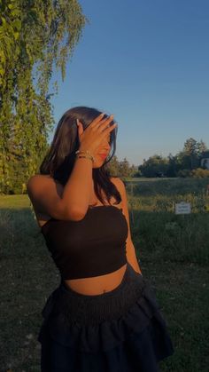 a woman in a black top is covering her face with her hands and looking into the distance