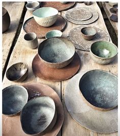 many bowls and spoons are sitting on a wooden table with different colored plates around them