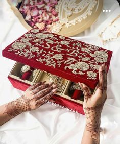 a woman is holding a red box with gold designs on it and her hands are touching the lid