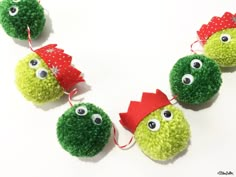 three green balls with googly eyes and red bows are hanging on a white surface