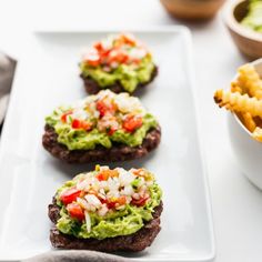 three burgers with guacamole, tomatoes and onion on them are served next to fries