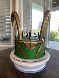 a green and gold decorated cake sitting on top of a wooden table next to a window