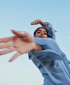 a woman wearing a blue hijab reaching up to catch a frisbee