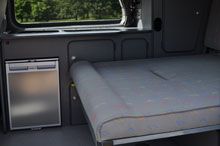 an empty bed in the back of a van with a window open and trees outside