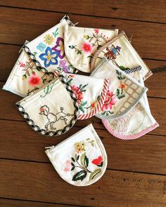 six embroidered pot holders on a wooden surface with one folded up and the other closed