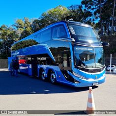 a blue double decker bus parked in a parking lot next to a cone with people standing around it