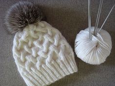 two white knitted hats with pom - poms next to each other on the floor