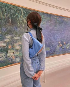 a woman standing in front of a painting with a back pack on her shoulder and looking at it