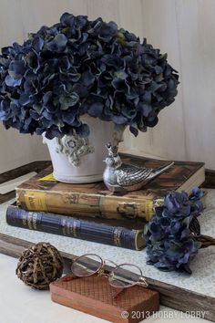 a vase filled with blue flowers sitting on top of two books next to a bird figurine