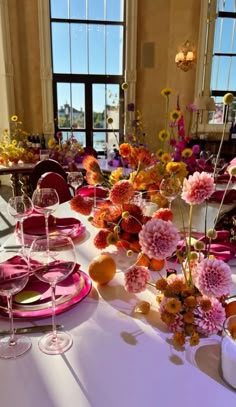 the table is set with plates, glasses and vases filled with different colored flowers