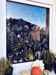 pumpkins and gourds are sitting in front of a window with chalk drawings on it