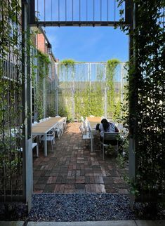 an open patio with tables and chairs in the middle, surrounded by greenery on both sides