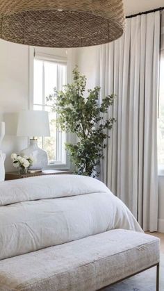 a bed with white linens and pillows in a bedroom next to a plant on a table