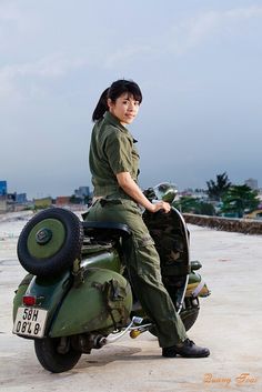 a woman in uniform sitting on the back of a green motorbike while posing for a photo