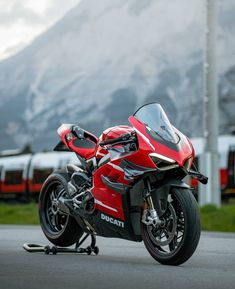 a red and black motorcycle parked on the street next to a train track with mountains in the background