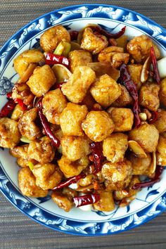 a blue and white bowl filled with fried food on top of a wooden table next to chopsticks