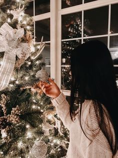 a woman standing in front of a christmas tree holding an item up to her face