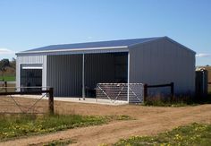 a large metal building sitting on top of a dirt road next to a lush green field