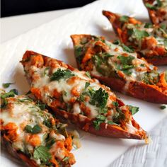 four pieces of baked sweet potatoes with cheese and herbs on them sitting on a white plate