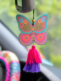 a colorful butterfly shaped keychain hanging from the side of a car window with tassels