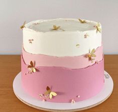 a three layer cake with pink and white frosting on a wooden table next to a wall