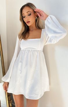 a woman wearing a white dress standing in front of a mirror with her hand on her head