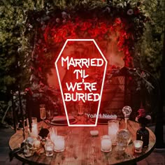 a wooden table topped with lots of candles next to a neon sign that says married in we're buried