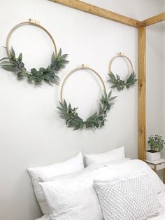 two wreaths hanging on the wall above a bed with white linen pillows and blankets